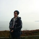 A young man in a hat holds a camera and smiles on a foggy overlook.